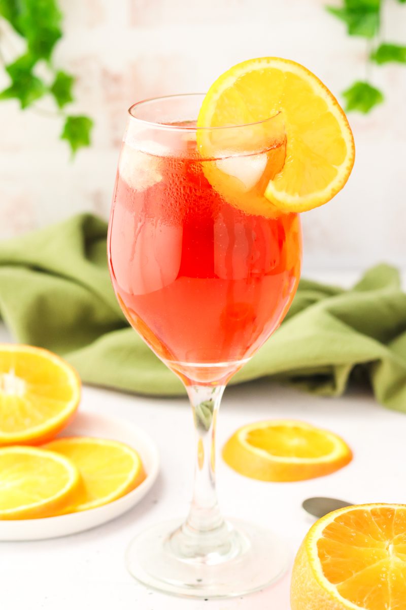 Tableview of an aperol spritz cocktail in a wine glass and garnished with an orange wheel. Hostess At Heart