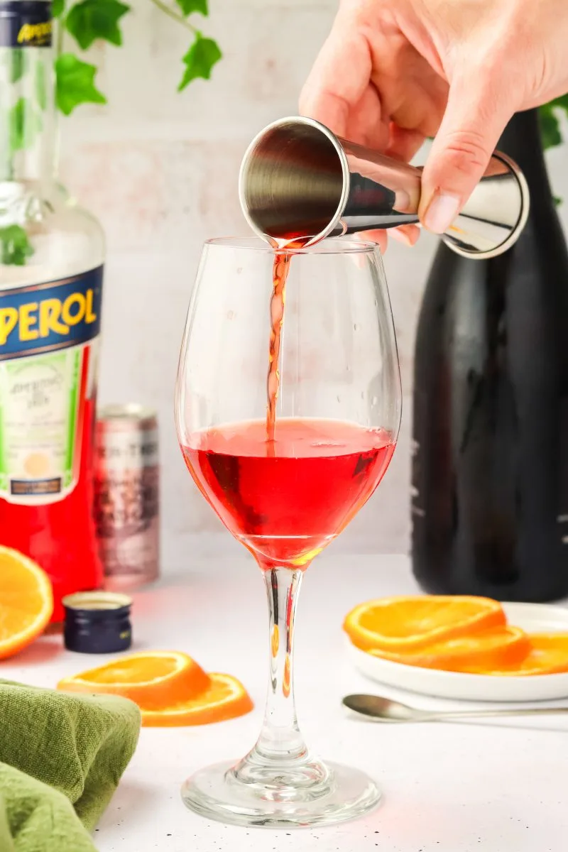 A jigger full of aperol being poured into a glass - Hostess At Heart