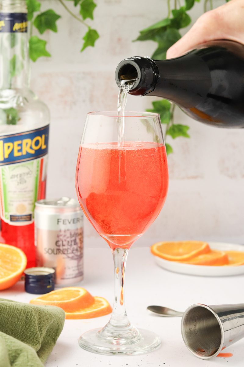 A glass of an aperol cocktail being topped off with prosecco - Hostess At Heart