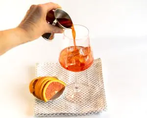 Aperol being added to prosecco in a large wine glass - Hostess At Heart