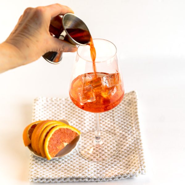 Aperol being added to prosecco in a large wine glass - Hostess At Heart