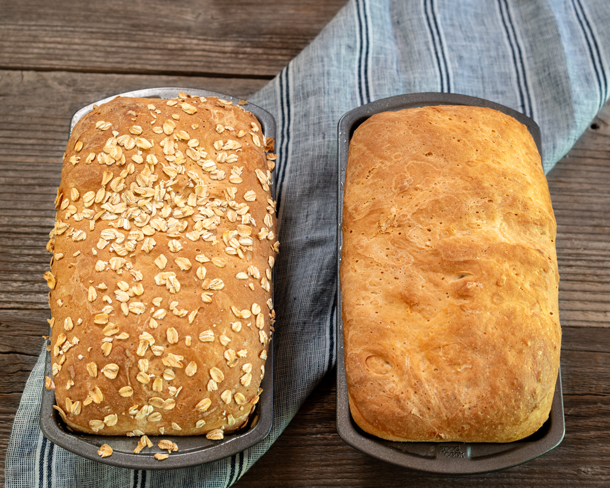 Top down image of two bread pans filled with golden brown English Muffin Bread, one topped with oats. Hostess At Heart