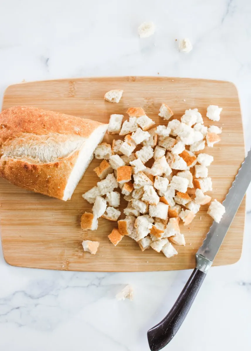 A loaf of bread on a cutting board being diced into cubes. Hostess At Heart