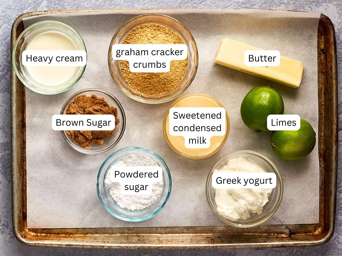 Labeled ingredients on a sheet pan in dishes including powdered sugar, greek yogurt, limes, sweetened condensed milk, brown sugar, heavy cream, graham cracker crumbs, and butter