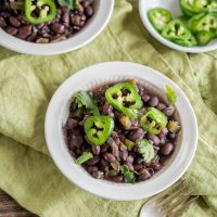 Top down view of a bowl of Cuban Black Beans garnished with slices of jalapenos and cilantro. Hostess At Heart
