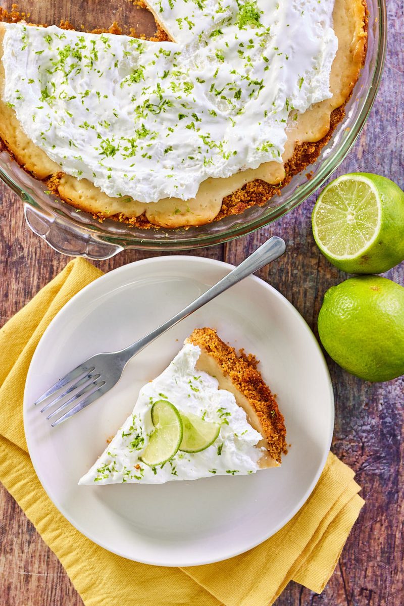 Top down view of a slice of pie garnished with lime zest in front of the whole sliced pie. Hostess At Heart