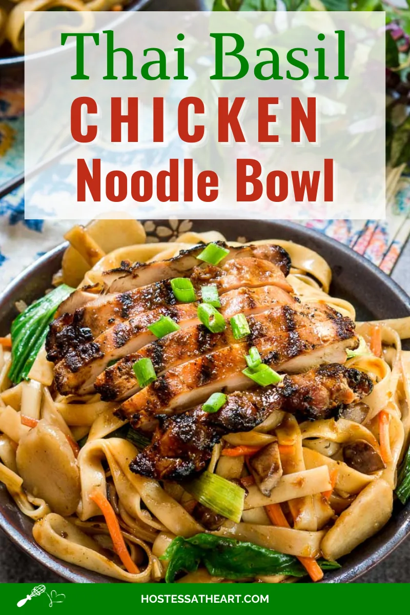 Side angle view of a dark gray bowl filled with noodles, carrots, and water chestnuts, sauced in Thai Basil flavors topped with grilled chicken- garnished with sliced green onions.