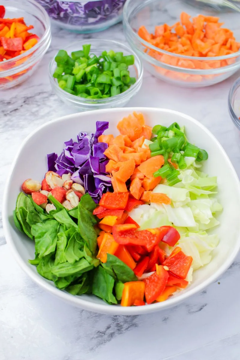 Angled view of a chopped salad filled with spinach and chopped vegetables with bowls of the ingredients in the background - Hostess At Heart