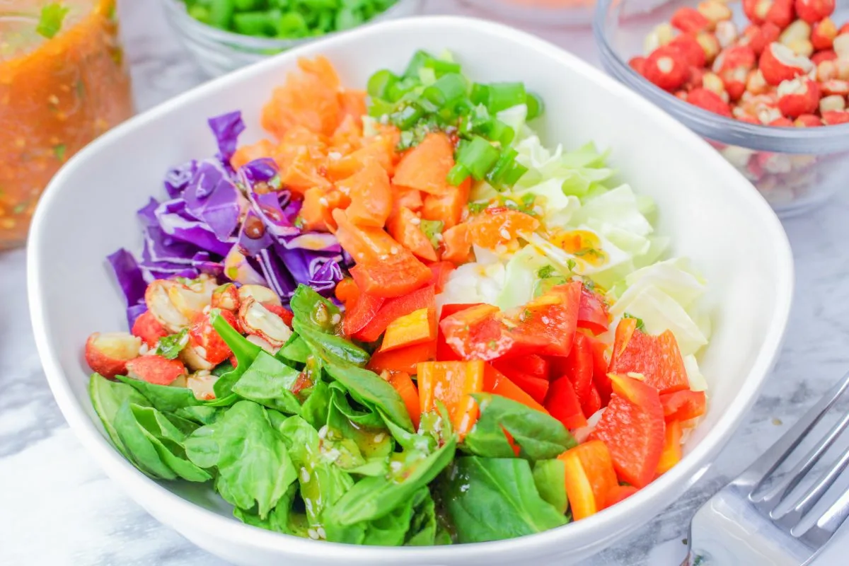 Angled view of a bowl of salad topped with chopped red peppers and purple cabbage. Hostess At Heart