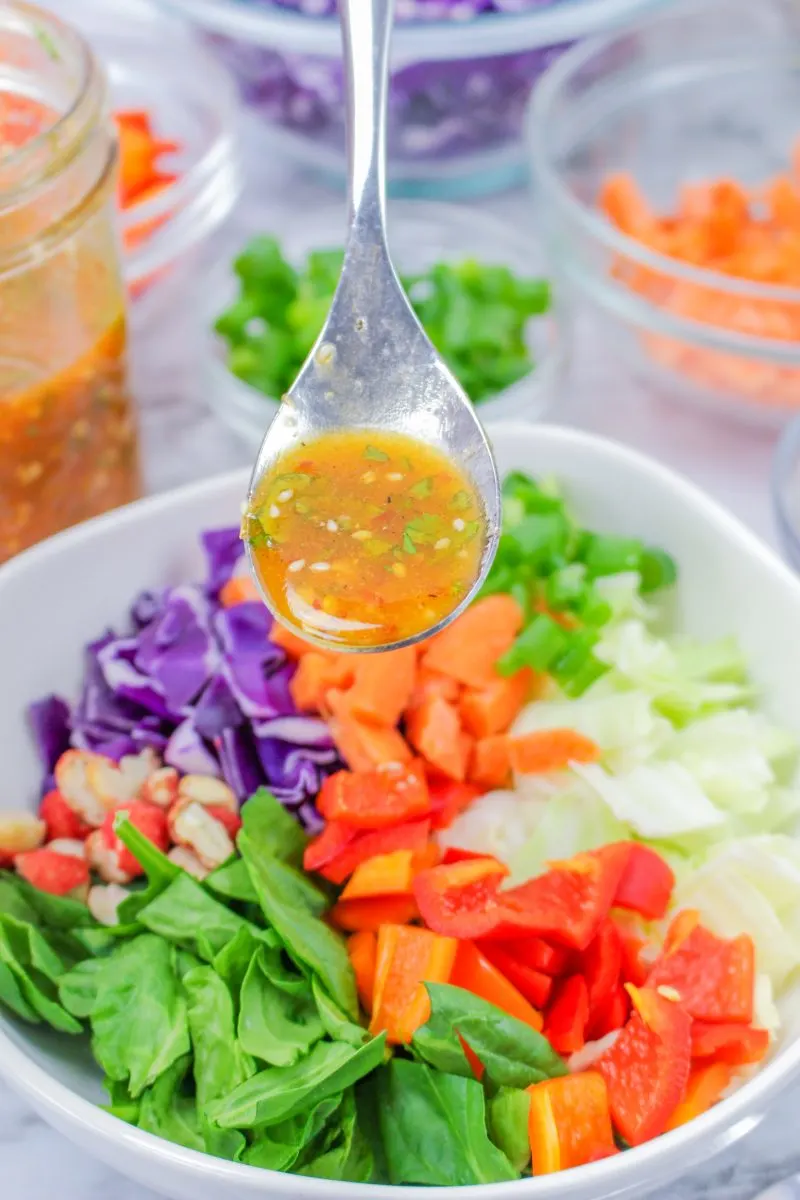 A spoon of Thai Dressing hovering over a bowl of Thai Salad - Hostess At Heart
