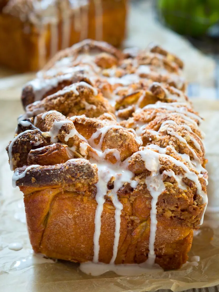 Tableview of a loaf of bread covered with streusel with glaze dripping down the sides - Hostess At Heart