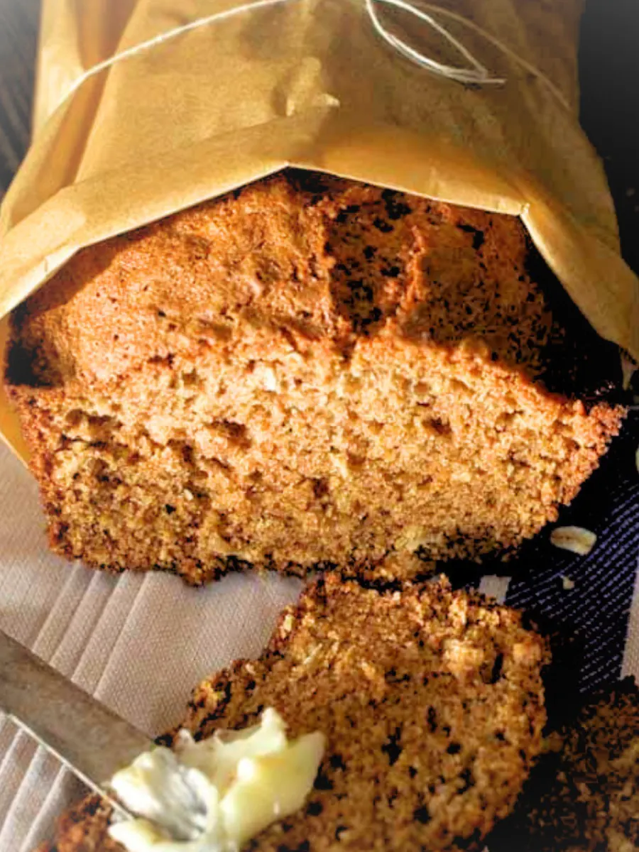 Top down view of a loaf of Oatmeal Applesauce bread with a buttered slice laying in the front - Hostess At Heart