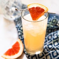 A sideview of a Grapefruit Crush Cocktail garnished with a wedge of grapefruit - Hostess At Heart