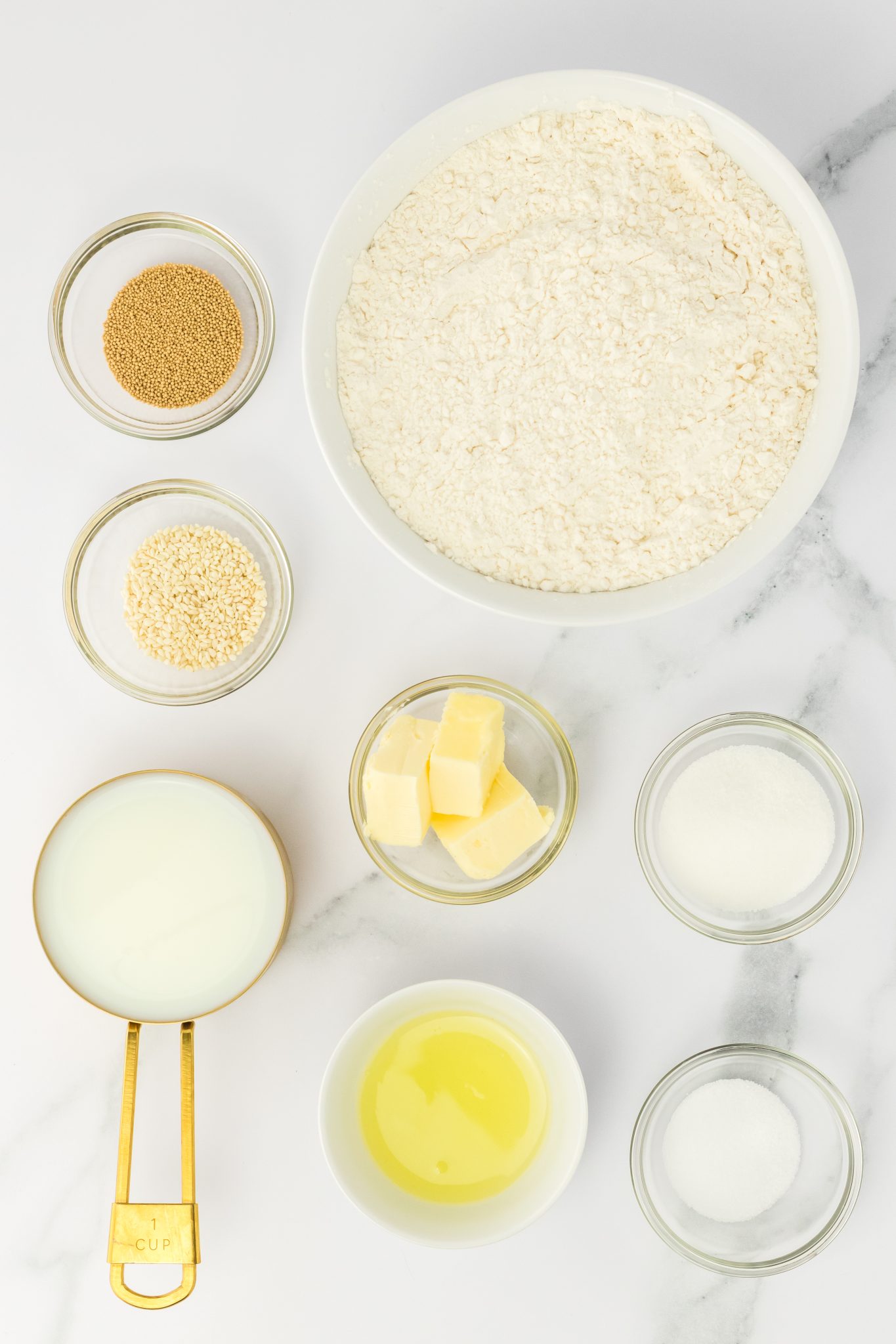 Top down view of ingredients. Yeast, flour, sugar, salt, butter, milk, sesame seeds and egg whites.