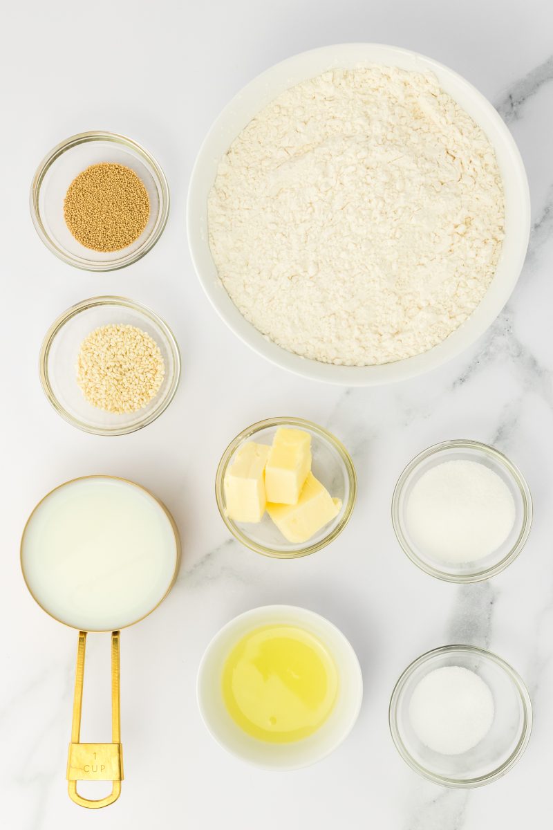 Top down view of ingredients. Yeast, flour, sugar, salt, butter, milk, sesame seeds and egg whites.