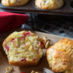 Close up image of a baked cranberry muffin cut in half and slathered in butter - Hostess At Heart