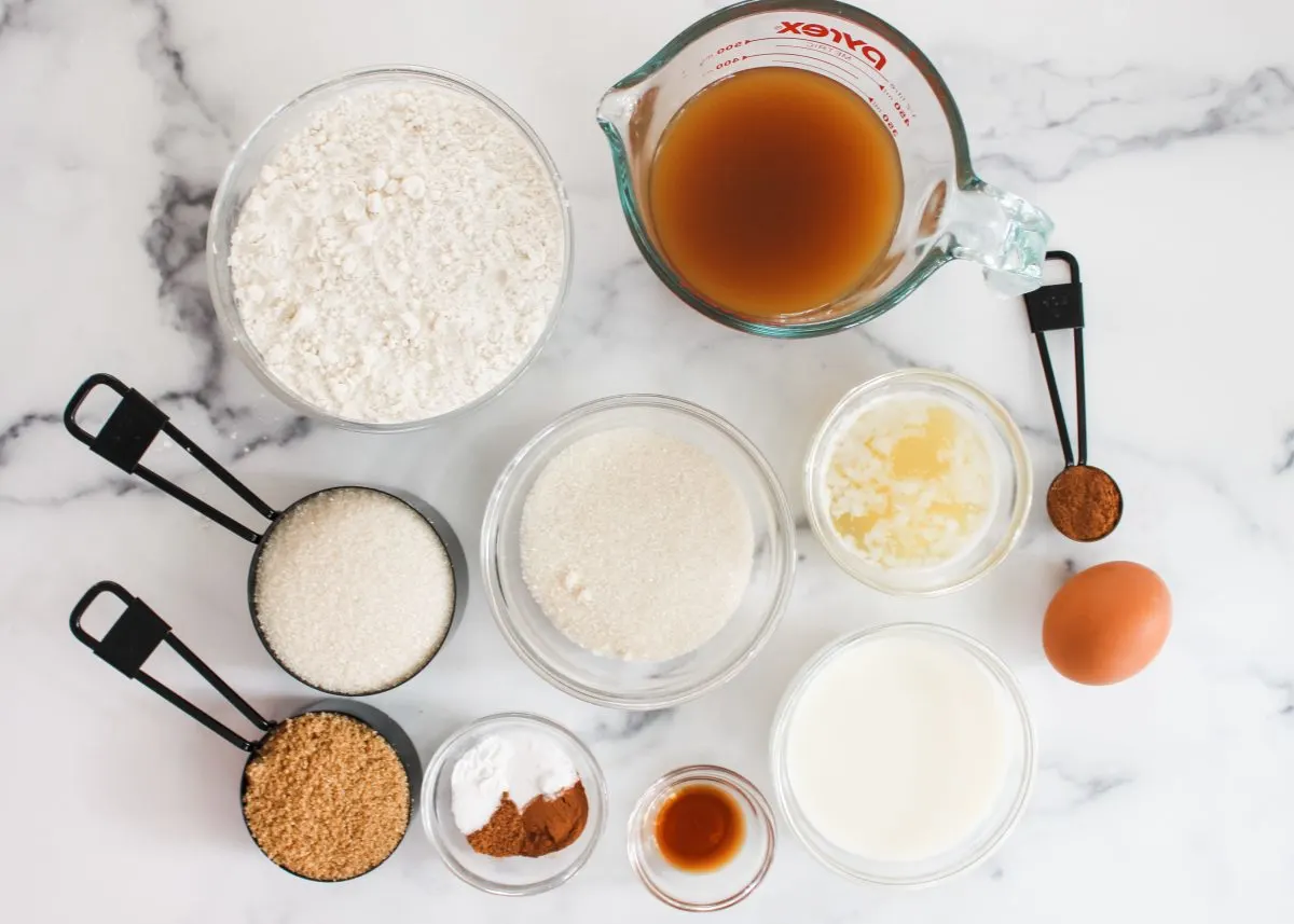 Top down view of the ingredients used to make apple cider donut muffin recipe including flour, sugar, cinnamon, butter, milk, butter, egg, apple cider, powdered sugar, and baking soda.