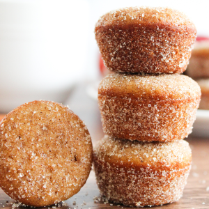 A stack of donut muffins covered in cinnamon and sugar. A muffin on it's side sits next to the stack. Hostess At Heart