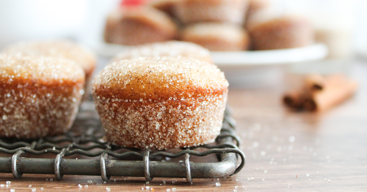 A sideview of donut muffins rolled in cinnamon and sugar sitting on a cooling rack. Hostess At Heart