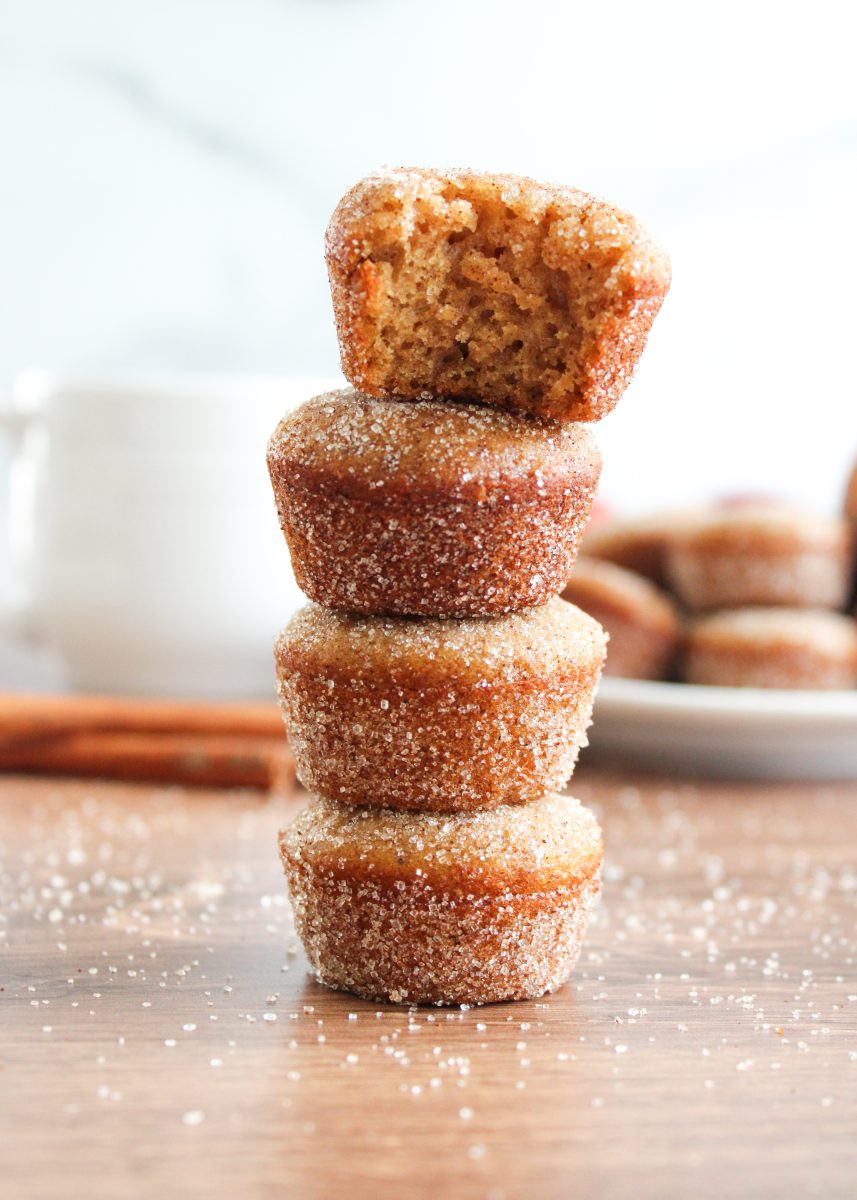 A stack of cinnamon and sugar coated mini muffins with a bite taken out of the top muffin.