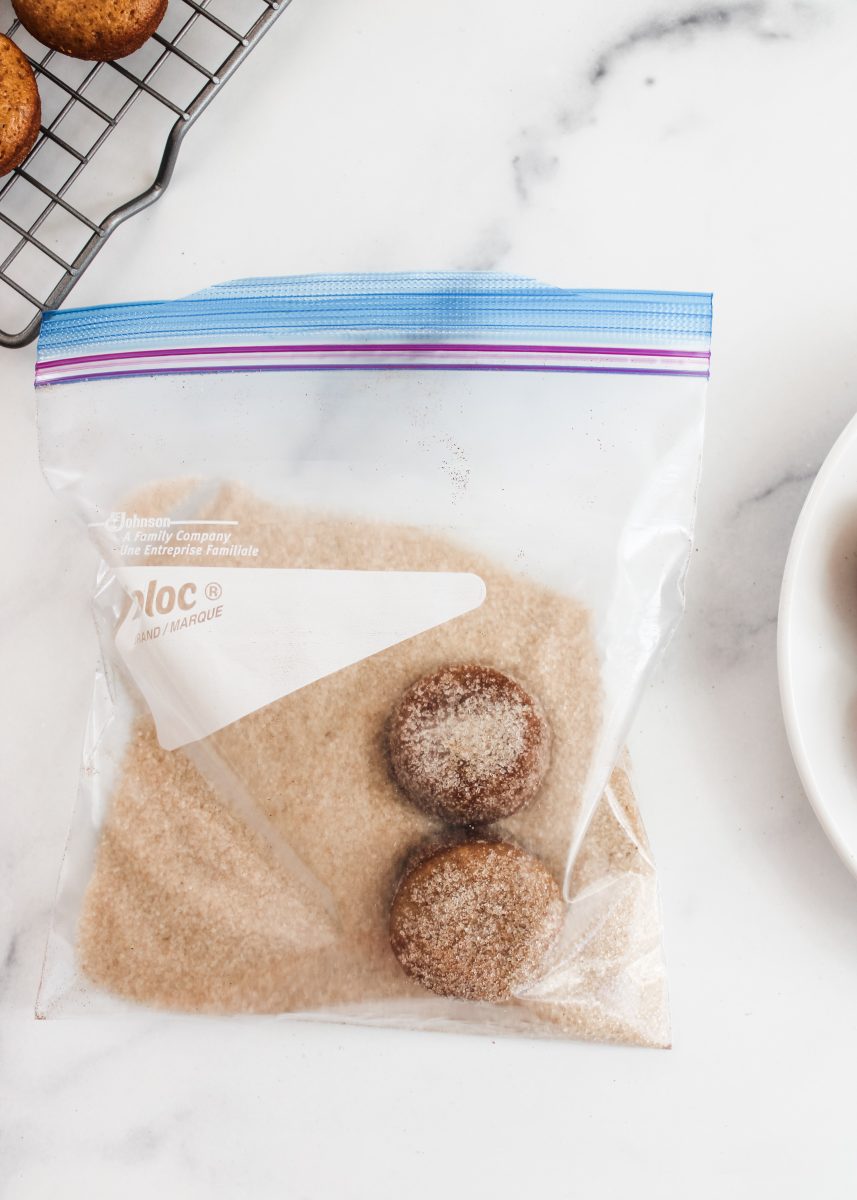 Two baked mini Apple Cider Donut Muffins in a bag of cinnamon and sugar. Hostess At Heart