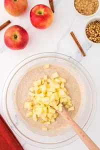 Muffin batter in a bowl topped with diced apples. Hostess At Heart