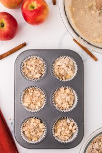 Top down view of a muffin pan filled with apple muffin batter topped with a nut streusel topping.