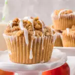 Sideview of a muffin sitting on a small stand topped with crumble and a glaze running down the side of the muffin - Hostess At Heart
