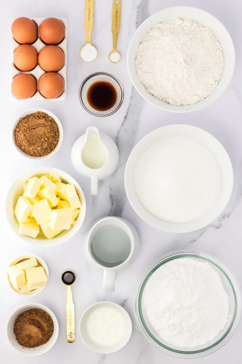 Top down view of chocolate buttermilk brownies and icing ingredients including butter, water, cocoa, powdered sugar, vanilla, water, sugar, flour, eggs, baking soda, salt, and buttermilk - Hostess At Heart