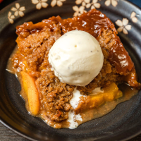 Top-down view of a slice of peach crisp topped with a scoop of ice cream. Hostess At Heart