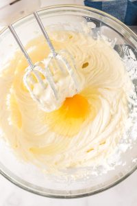 Egg added to beaten cream cheese filling in a bowl with an electric mixer. Hostess At Heart