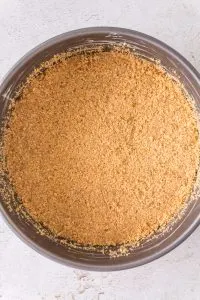 Graham cracker crust ingredients pressed into the bottom and up the sides of a springform pan - Hostess At Heart