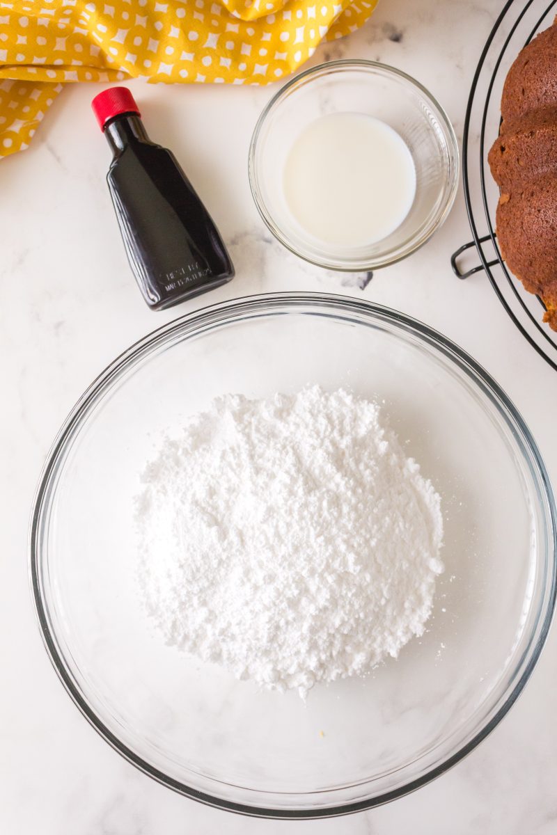 Top down view of ingredients used to make a sugar glaze including powdered sugar, vanilla, and milk.