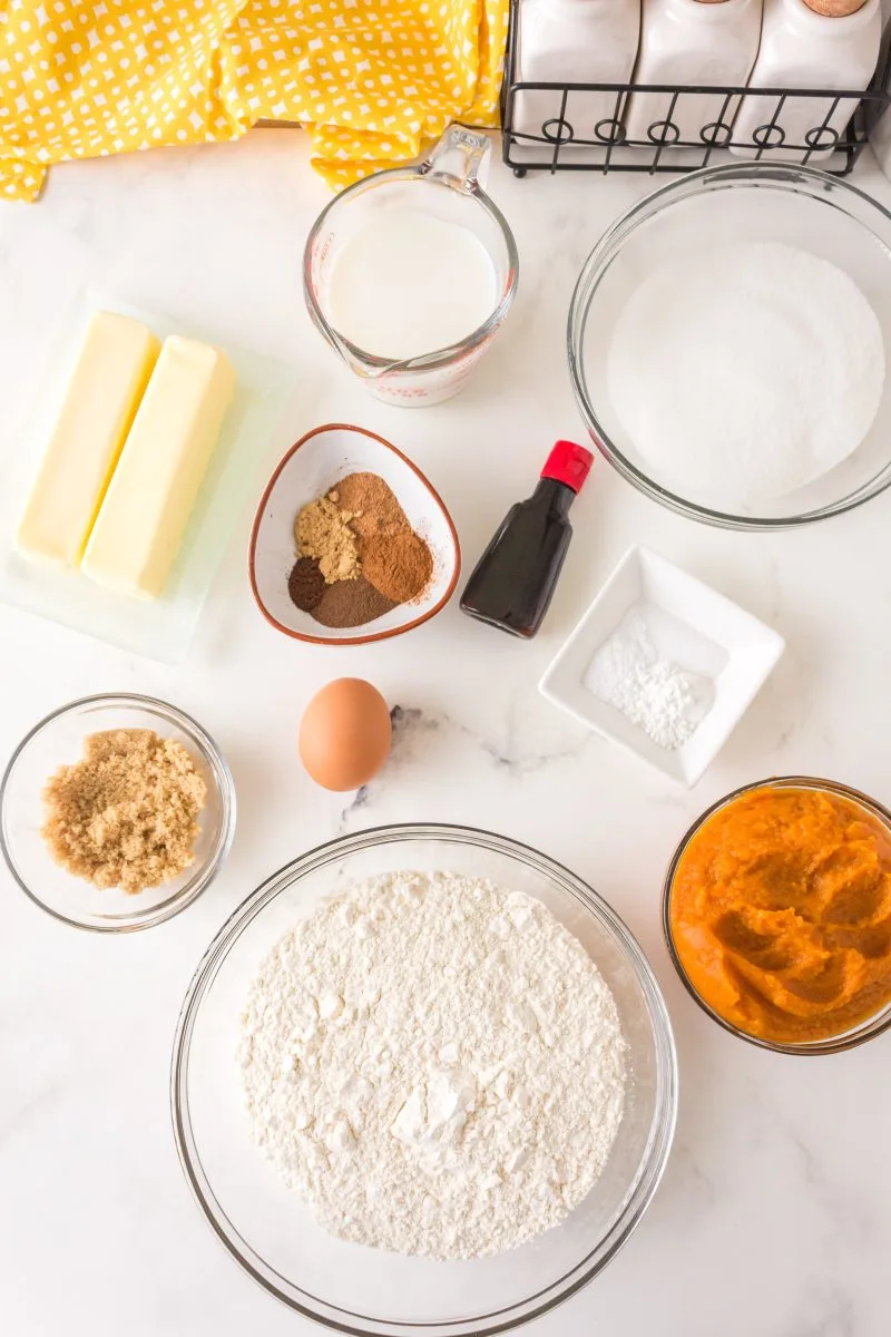 Top down view of pumpkin bundt cake ingredients including flour, pumpkin puree, brown sugar, egg, baking soda, butter, vanilla, milk, butter, baking powder, and spices.