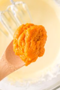 Spoonful of pumpkin puree being added to a cheese cake filling - Hostess At Heart