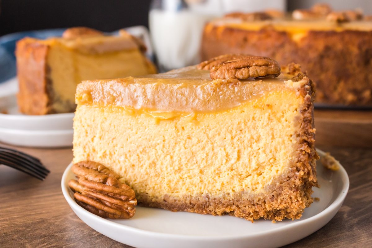 A sideview of a slice of pumpkin cheesecake with a graham cracker crust and a pecan praline topping.