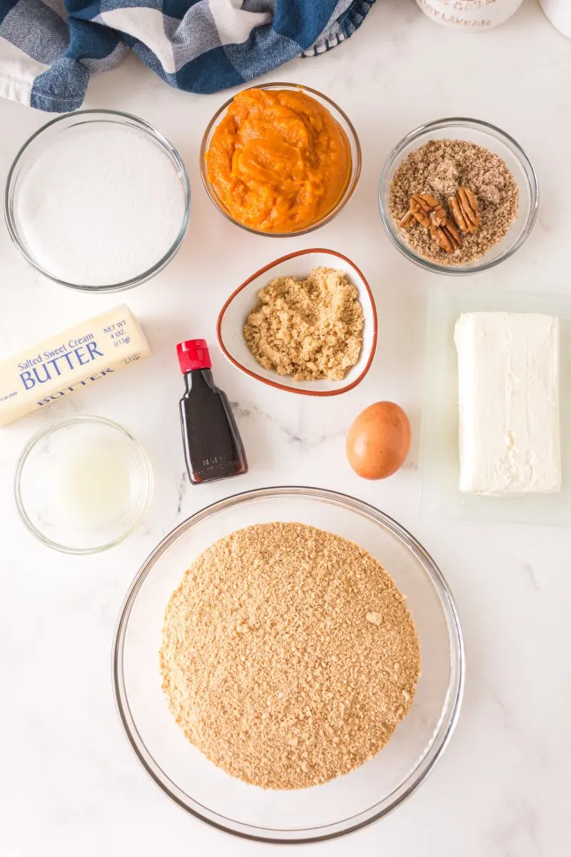 Ingredients needed to make pecan pumpkin cheese cake including graham cracker crumbs, butter, egg, vanilla, cream cheese, lemon juice, sugar, brown sugar, pecans and pumpkin puree.