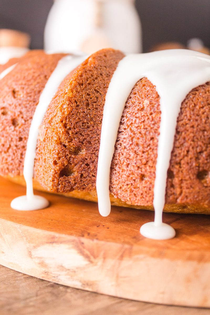 A sideview of a baked bundt cake with glaze dripping over the top - Hostess At Heart