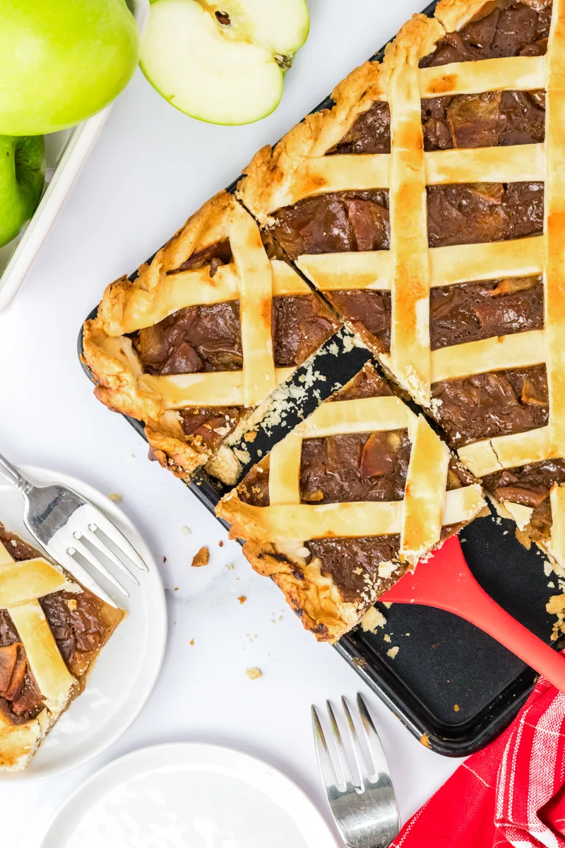 A sliced piece of apple slab pie being lifted from a baking sheet - Hostess At Heart