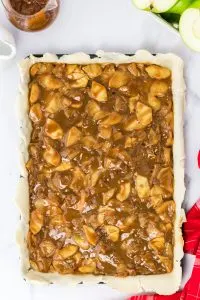 Caramel Apple Pie filling topped over a pie crust in a sheet pan - Hostess At Heart