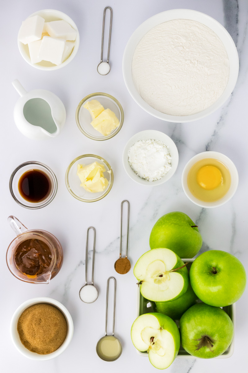 Top down view of ingredients including green apples, brown sugar, caramel, butter, vanilla, cinnamon, sugar, shortening, salt, egg, lemon juice, and cornstarch.
