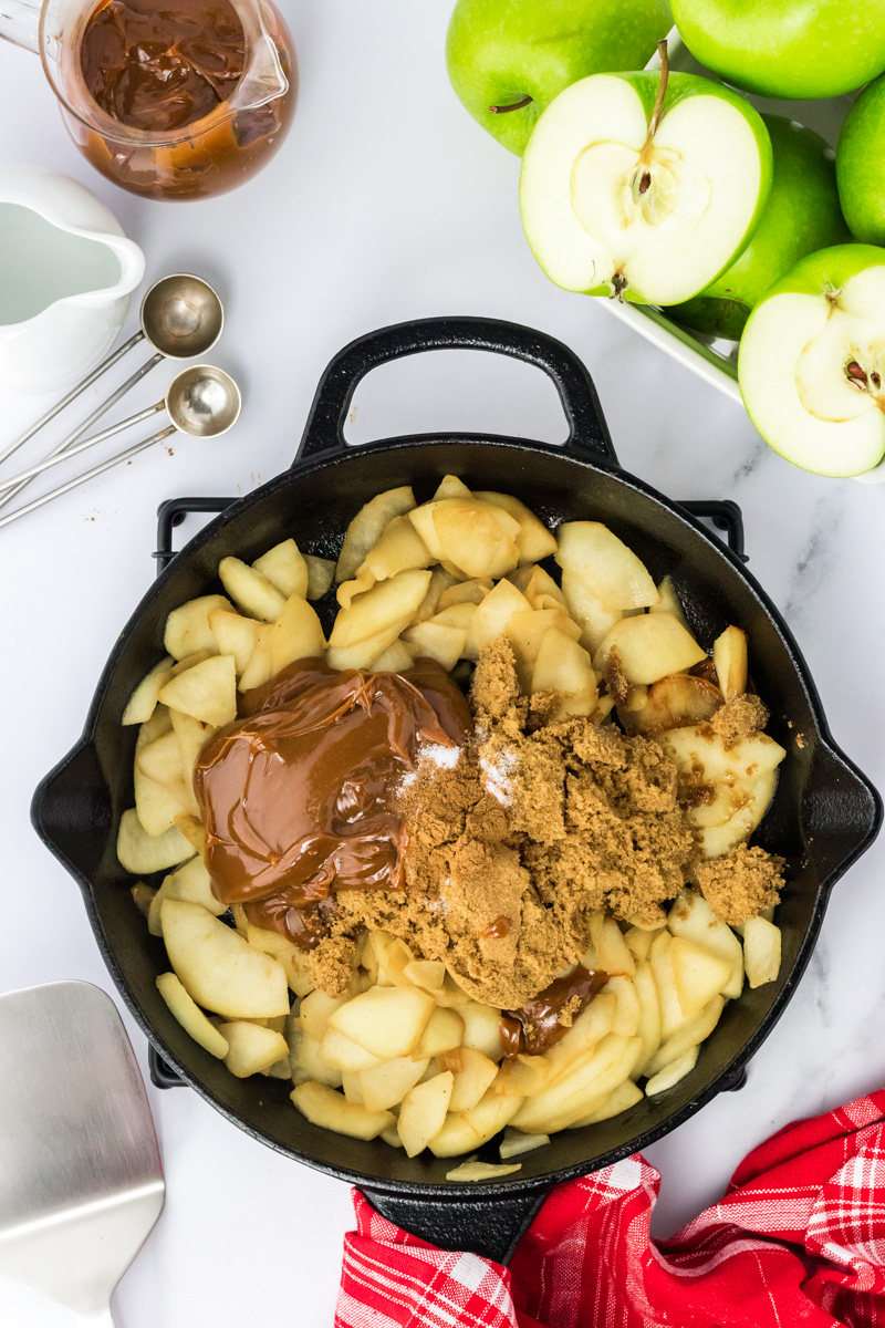 Top down view of a cast iron skillet filled with apples, brown sugar, caramel, and a pinch of salt - Hostess At Heart