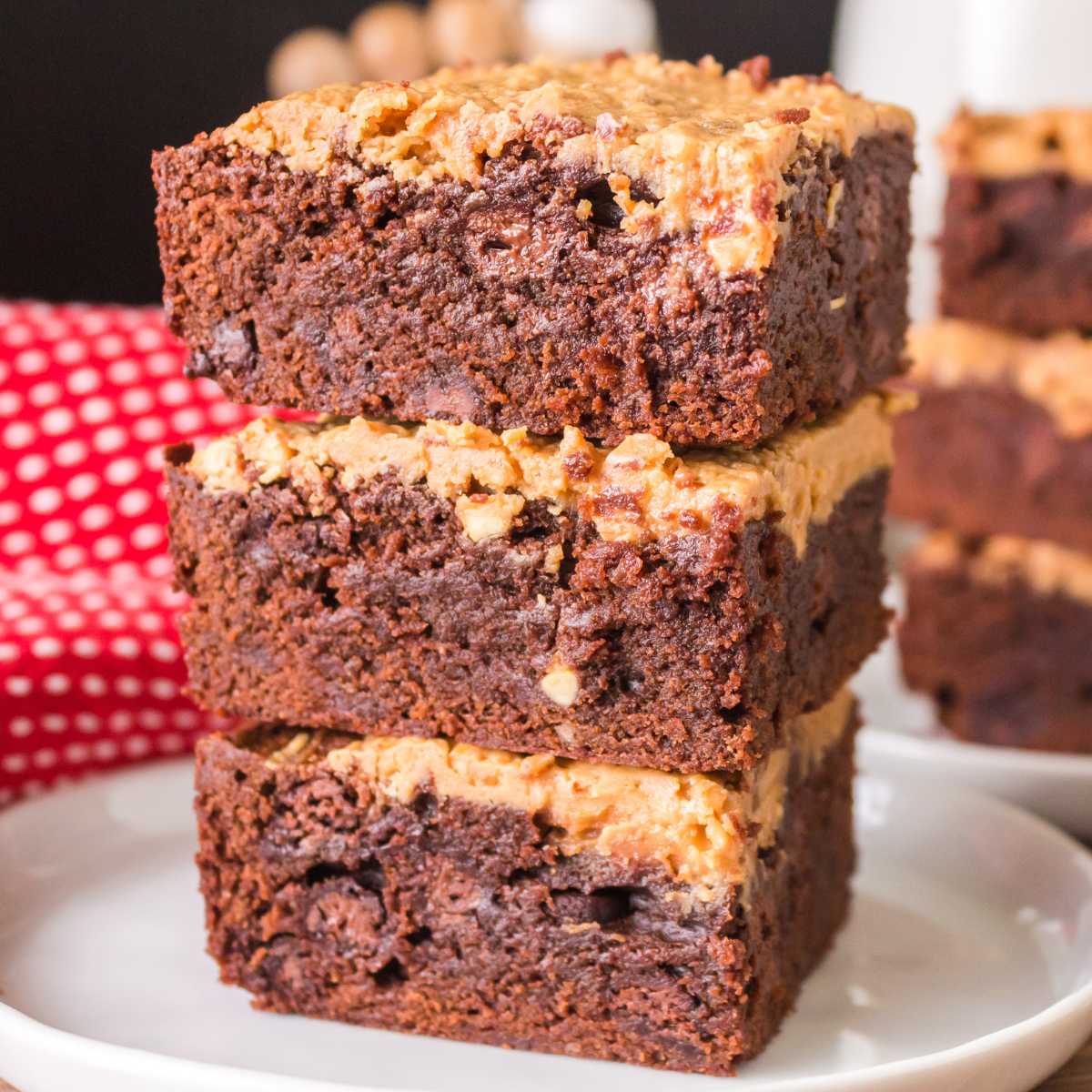 Side view of 3 moist fudgy chocolate brownies topped with a creamy peanut butter topping stacked on each other.