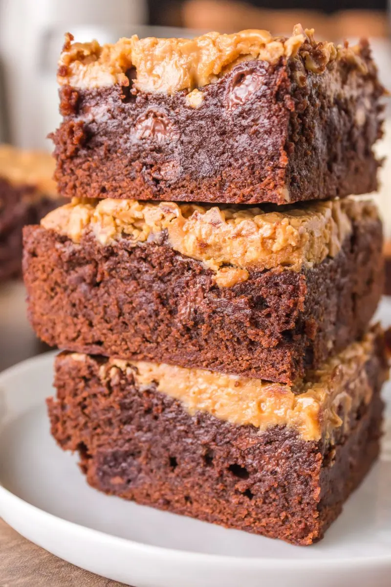 Close-up sideview of three chocolate brownies topped with a crunchy peanut butter layer stacked on each other - Hostess At Heart