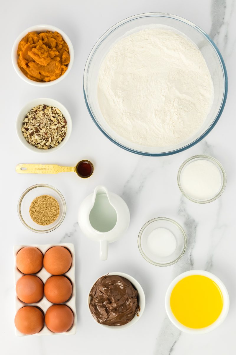 Top down view of the ingredients needed to make pumpkin babka including butter, Nutella, eggs, flour, sugar, yeast, salt, vanilla, hazelnuts, and pumpkin - Hostess At Heart