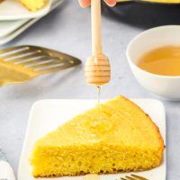 A honey spoon drizzling honey over a wedge of cornbread - Hostess At Heart