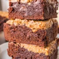 Close-up sideview of three chocolate brownies topped with a crunchy peanut butter layer stacked on each other - Hostess At Heart