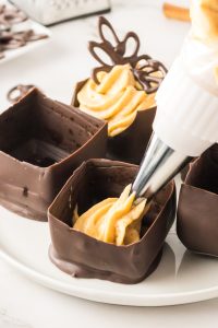 A piping bag filling a mini chocolate cup with pumpkin mousse - hostess at heart