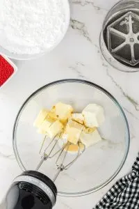 Cubes of cream cheese and butter being whipped together with vanilla with an electric mixer in a bowl. Hostess At Heart