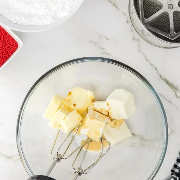 Cubes of cream cheese and butter being whipped together with vanilla with an electric mixer in a bowl. Hostess At Heart